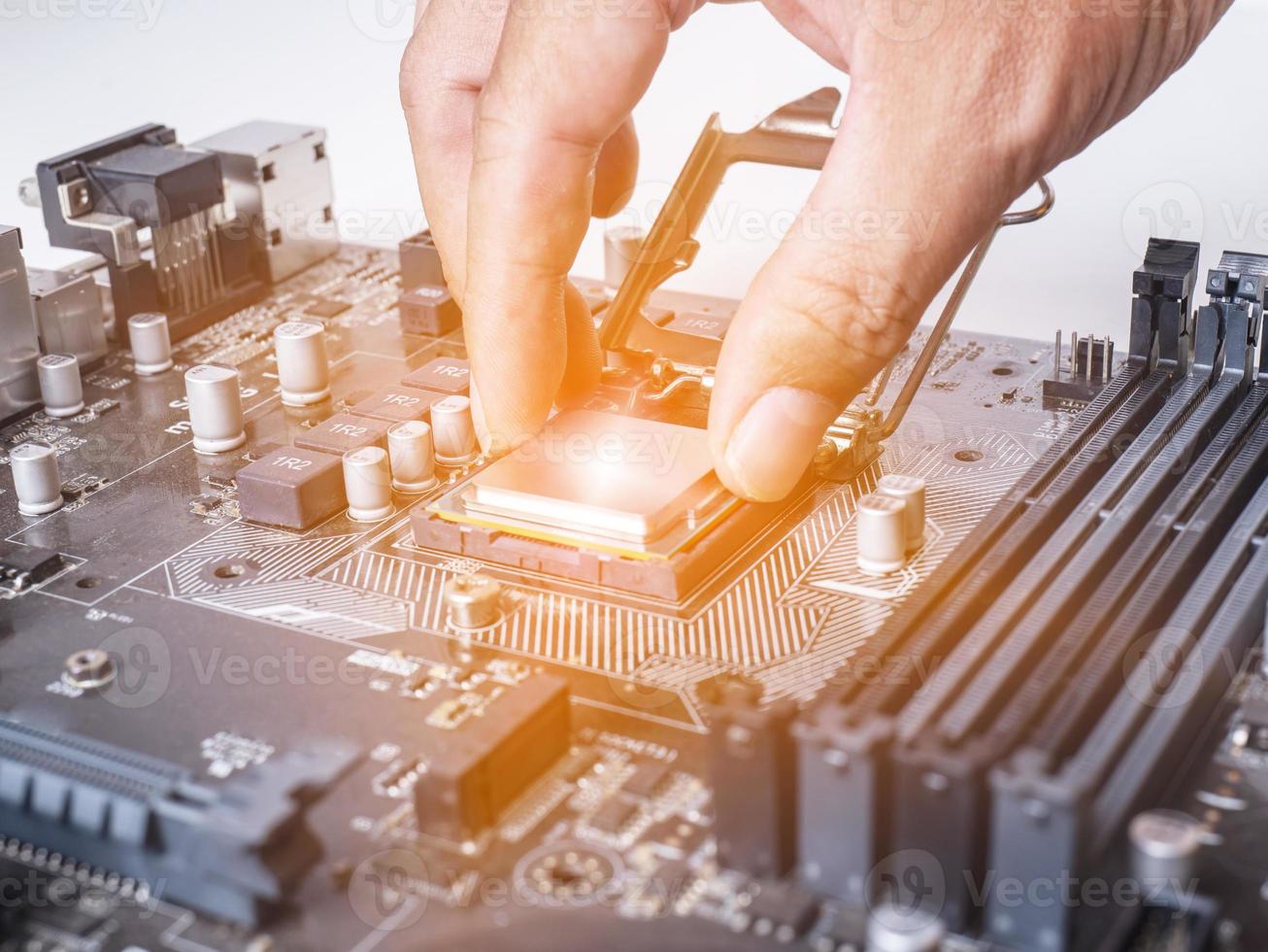 Hold the CPU handle and insert it into the CPU slot on the motherboard. It's an old motherboard, lots of dust. Put orange light on the cpu slot. There is a RAM slot next to it. There is a capacitor. photo