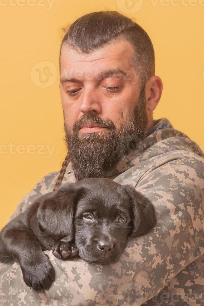 Man in military clothes with a Labrador Retriever puppy in his arms. Man and dog. photo