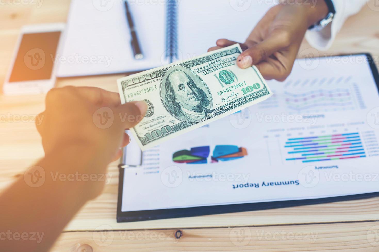 Business woman gripping The United States hundred-dollar bills in her hand and some put on the table full with business charts and notebook photo