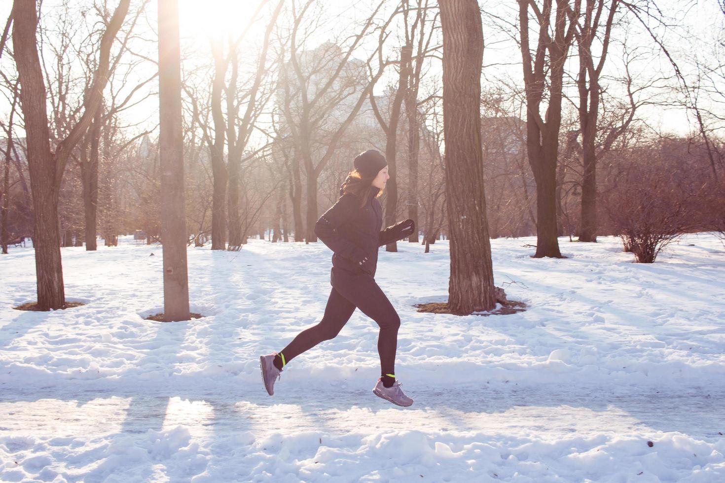 young woman athlete in black sport suit run in winter park photo