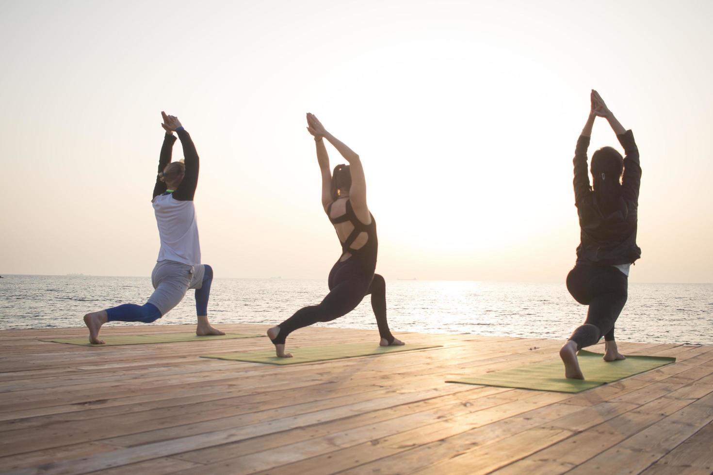 group of womans and man doing yoga on wooden pier, morning sea background photo