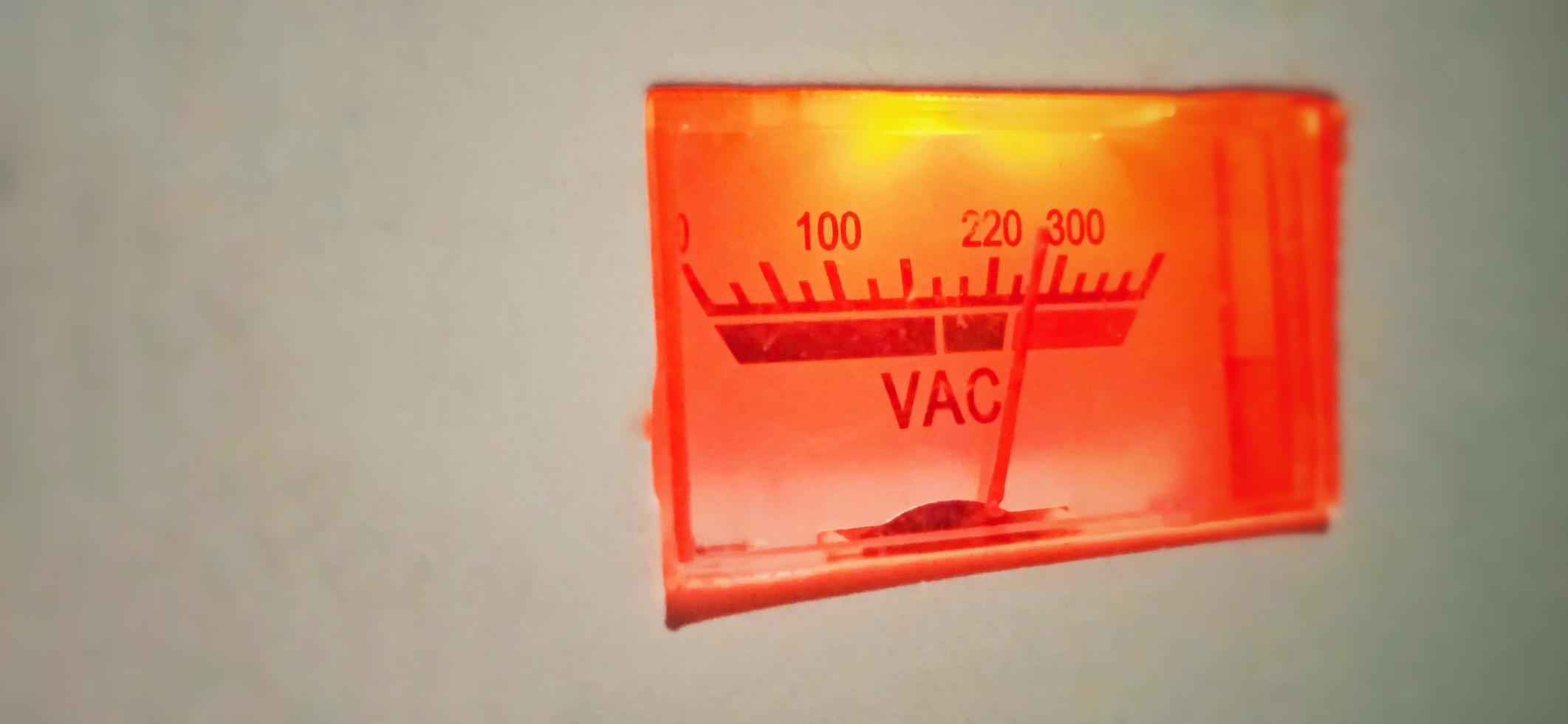 An isolated red-orange old volt ampere meter electrical equipment display under dim condition. photo