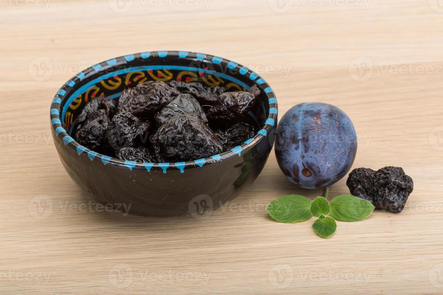 Dried plums in a bowl on wooden background photo