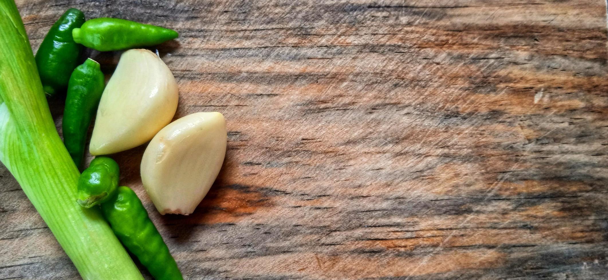 Vegetables of leek, garlic, and green chilli on the wooden cutting board. Vegetables ingredient background design. Suitable for advertising of food, drink, poster, backdrop, food company and industry. photo
