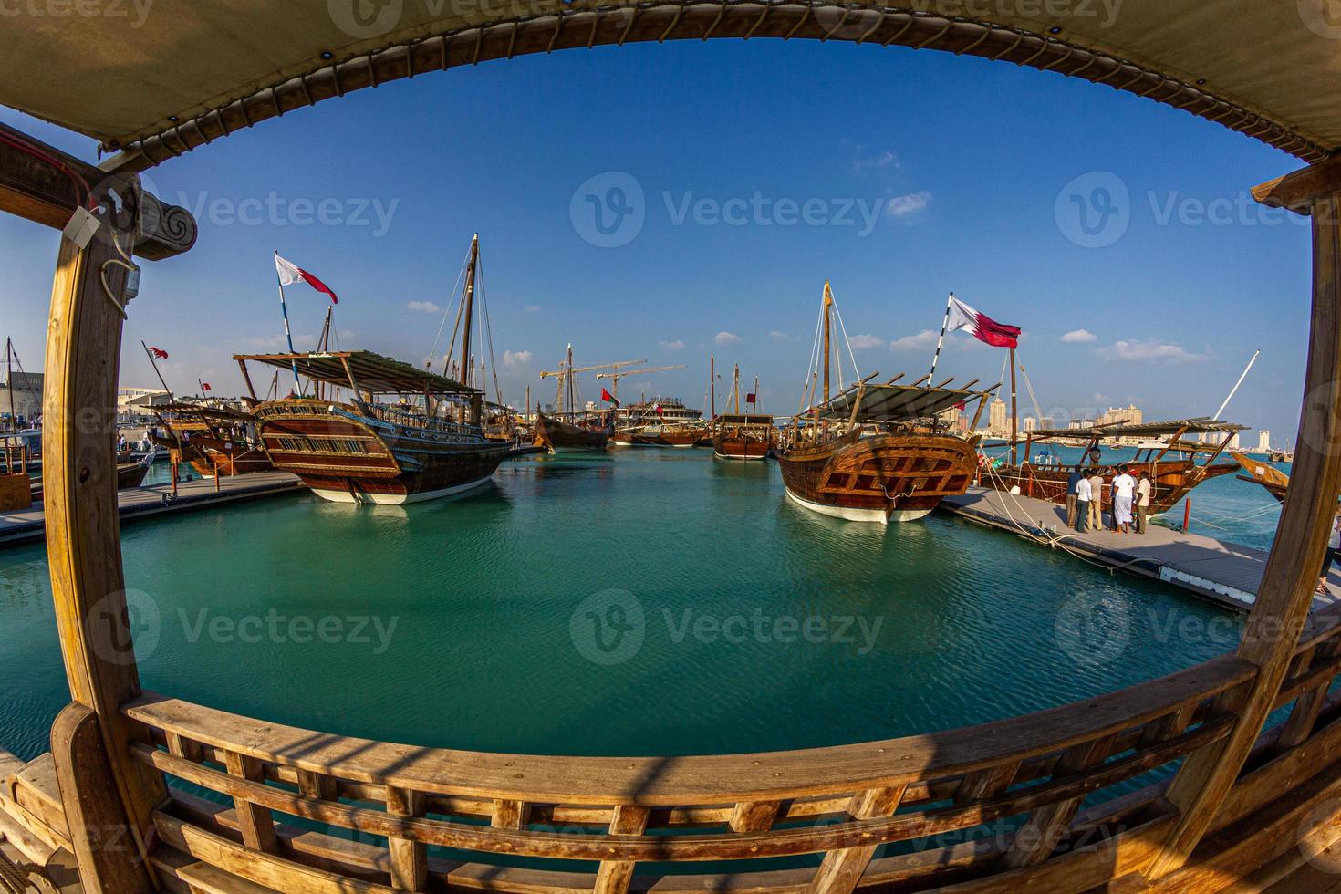 Traditional wooden boats ,dhows, in Katara beach Qatar daylight view with Qatar flag and clouds in sky photo