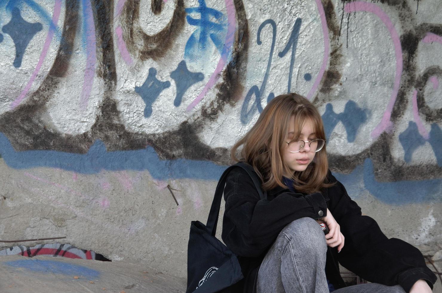 St. Petersburg, Russia, 06.01.2022. A teenage girl sits in an abandoned building painted with graffiti and smokes photo