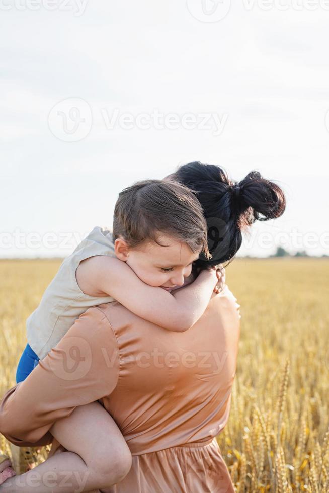 Happy family of mother and infant child walking on wheat field, hugging and kissing photo