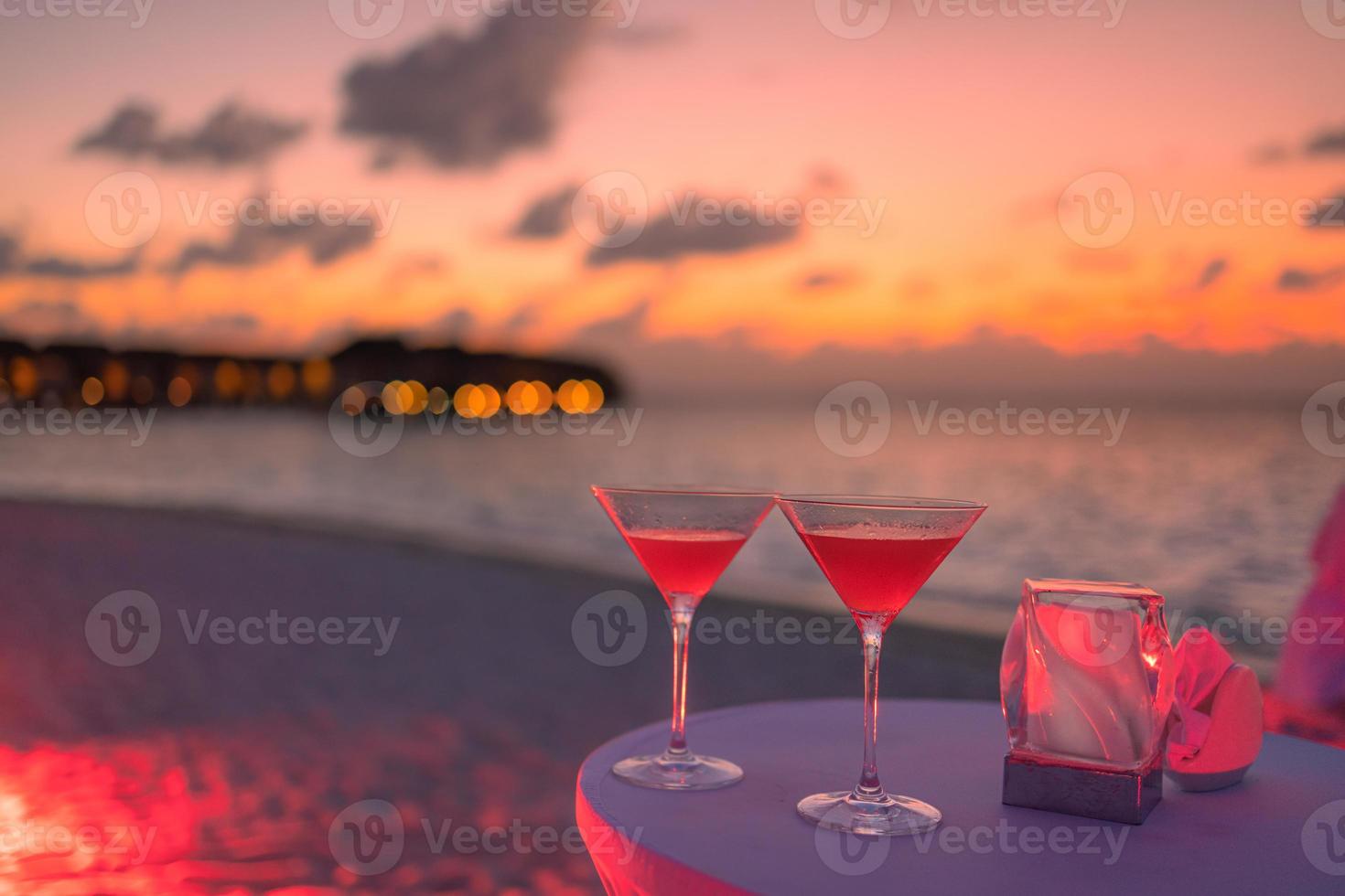 dos cócteles con gente de fiesta en la playa borrosa y un colorido cielo de puesta de sol en el fondo. estilo de vida de lujo al aire libre, colores relajantes y románticos, gente borrosa de fiesta en una noche de verano foto