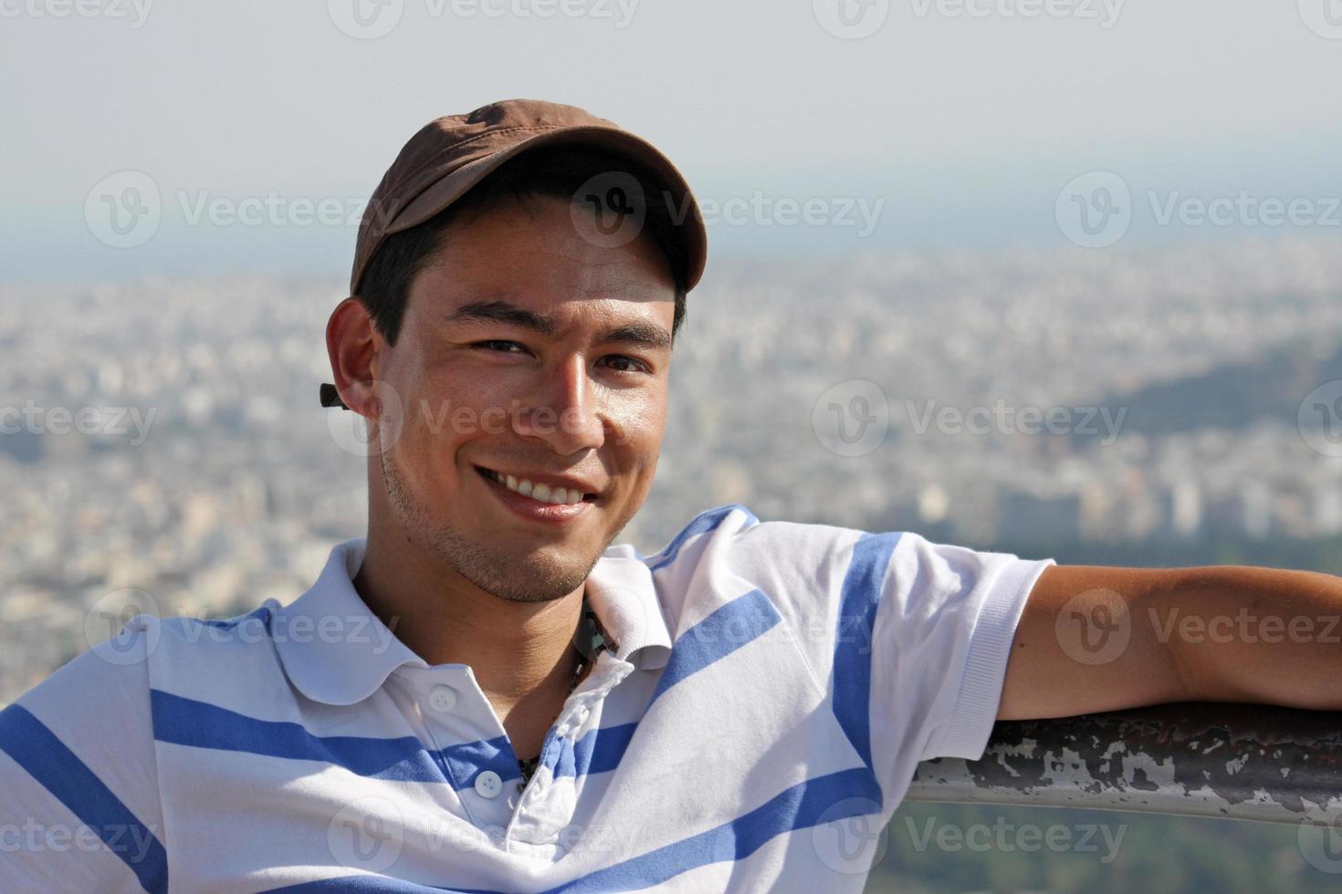 apuesto y sonriente joven sentado al sol con la ciudad de atenas, grecia, en el fondo foto