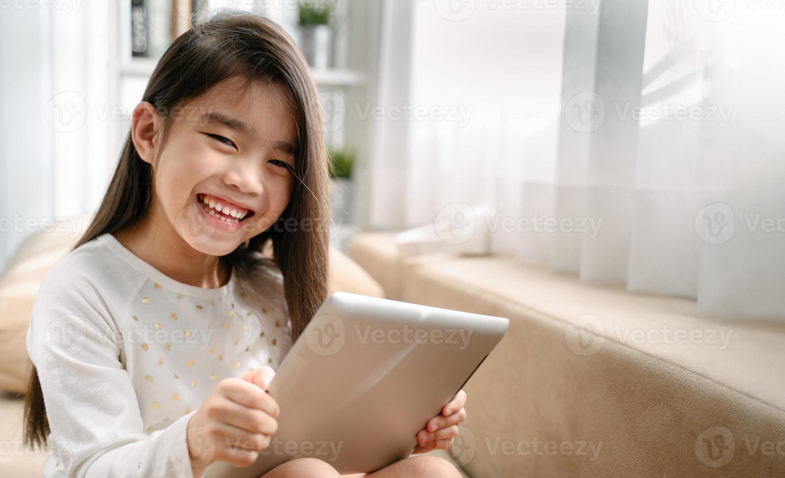 asian little girl playing with smartphone, technology and communication concept - smiling girl texting on smartphone and lying in bed at home photo