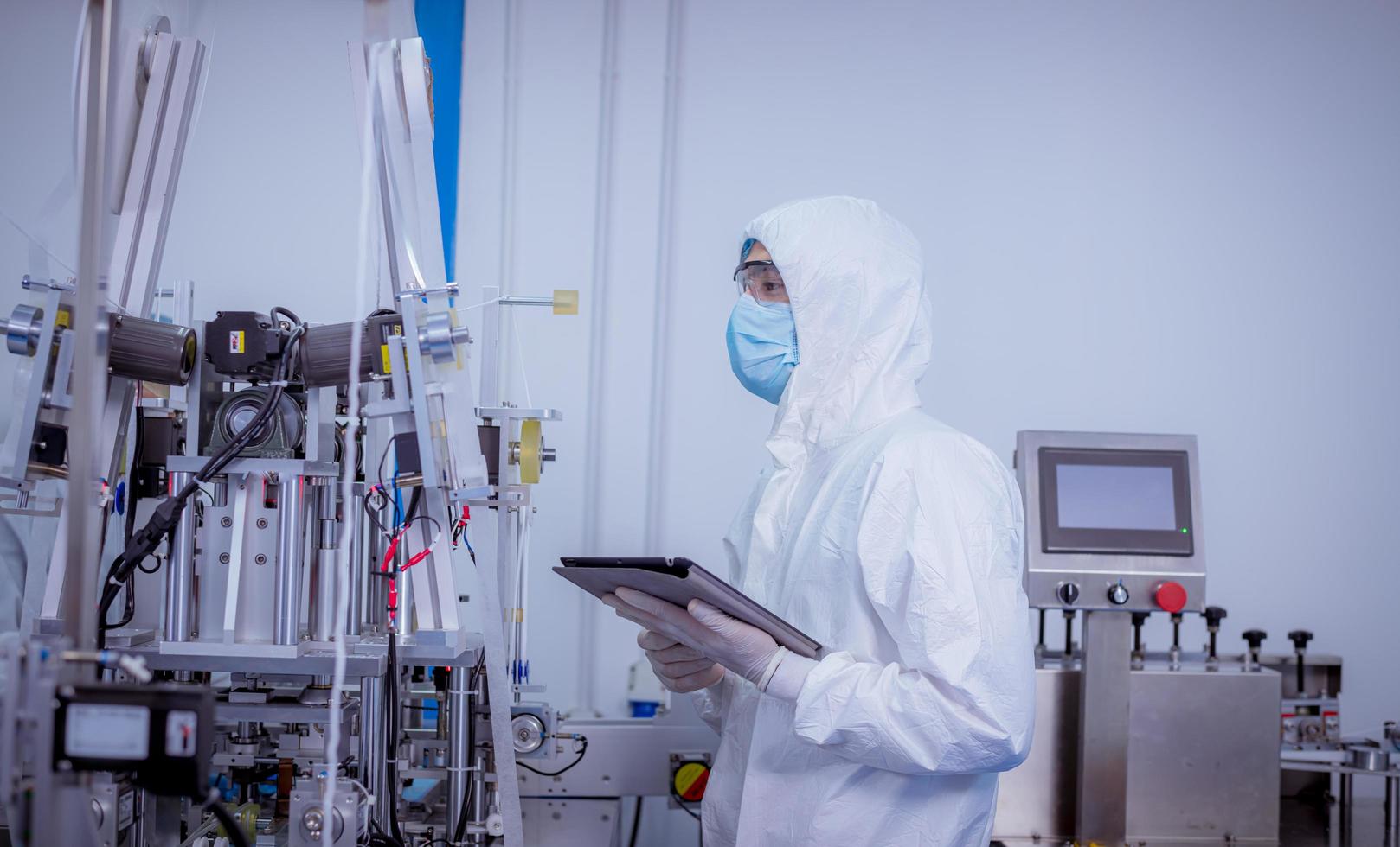 Technician worker wearing protective suite , glove are inspect machine with check  face mask manufacturing process to safe and against from virus photo