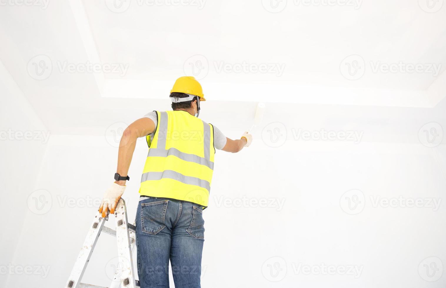 A view of the painter behind the wall painter with a paint roller and split bucket on a large empty space with a wooden staircase. photo