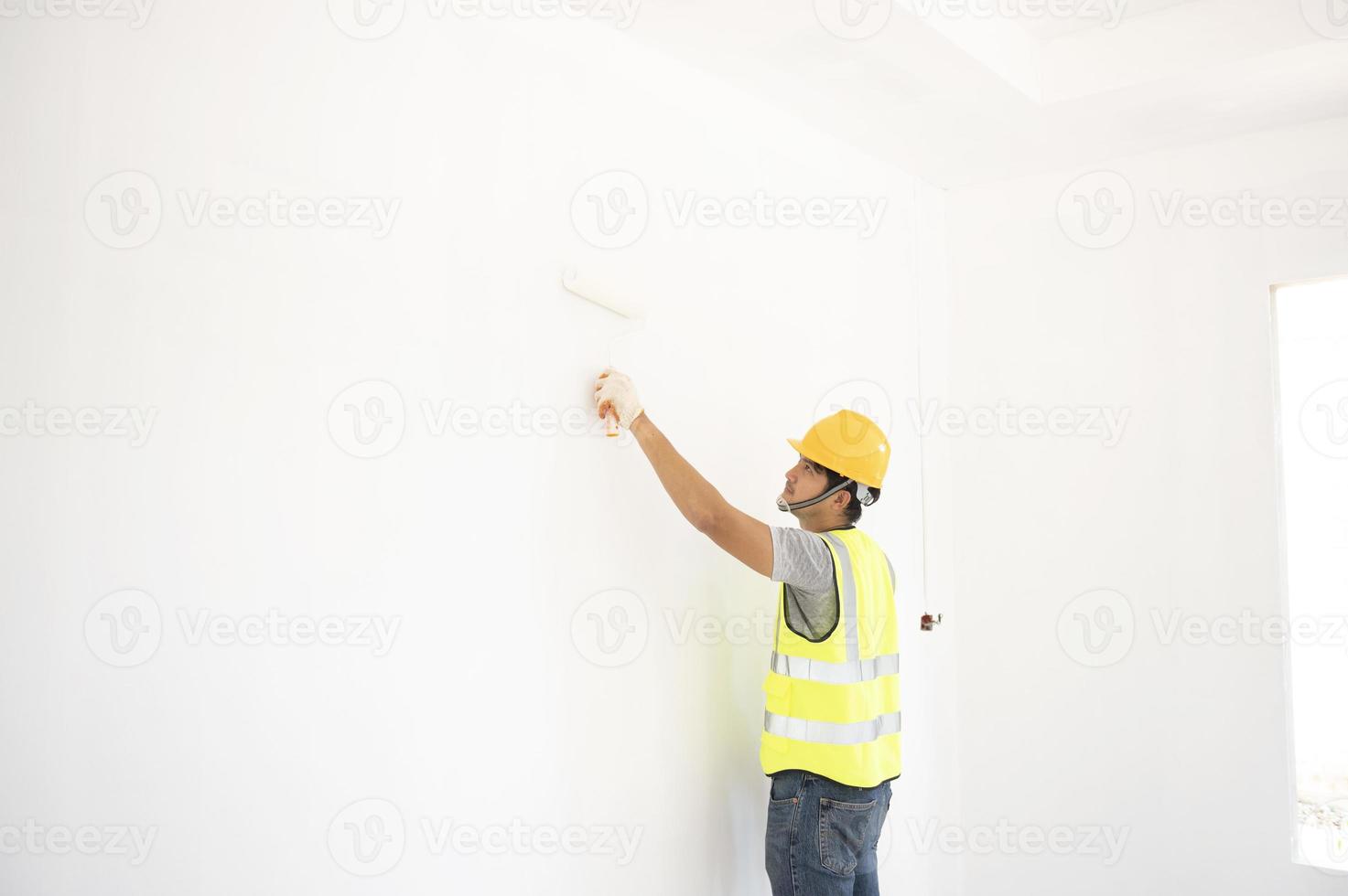 A view of the painter behind the wall painter with a paint roller and split bucket on a large empty space with a wooden staircase. photo