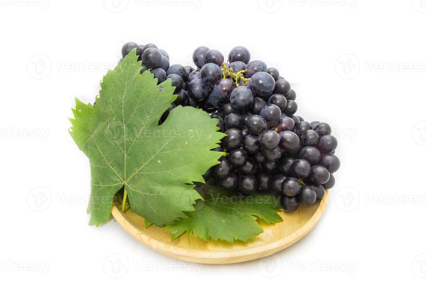 Black grapes bunch isolated on wooden plate and white background with green leaf package design element photo