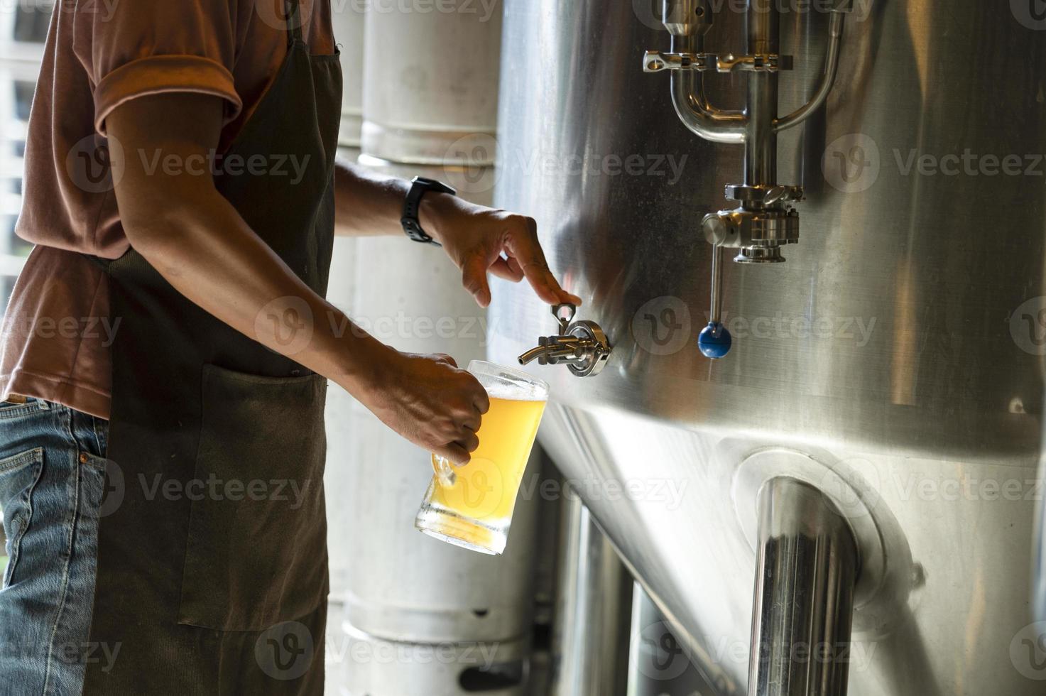 A young man works in a brewery and checks the quality of craft beer. The brewery owner tastes the best beers from Bach. A man's shortcut fills a glass of beer with photo