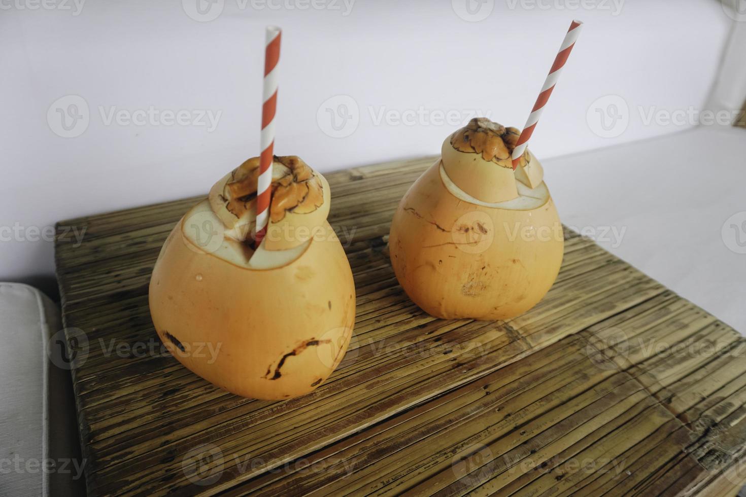 two coconut juices with paper straws placed on a wooden table photo