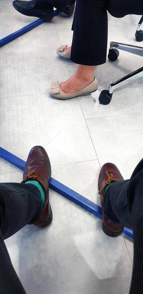 Leg of businessman and woman under table with white floor or tile background. Bottom view of brown and cream leather shoes with black pants. photo