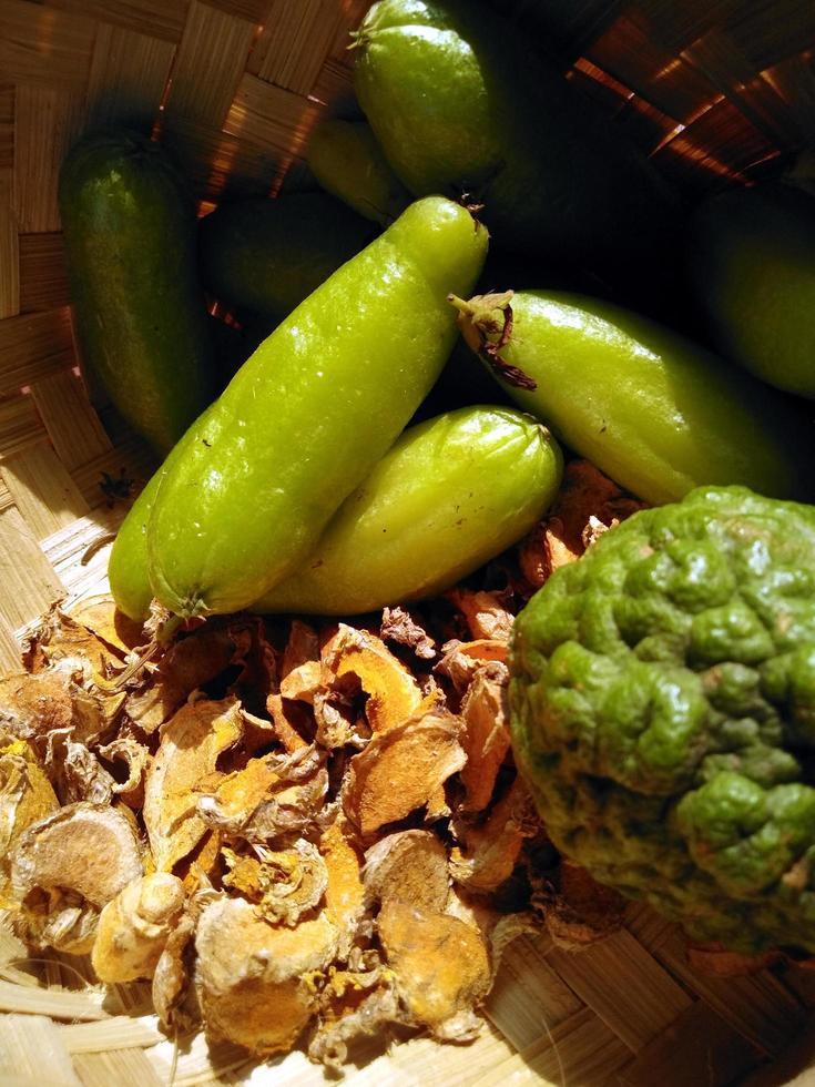 a variety of spices for cooking served in a woven bamboo container such as turmeric, ginger, bilimbi and lime. photo