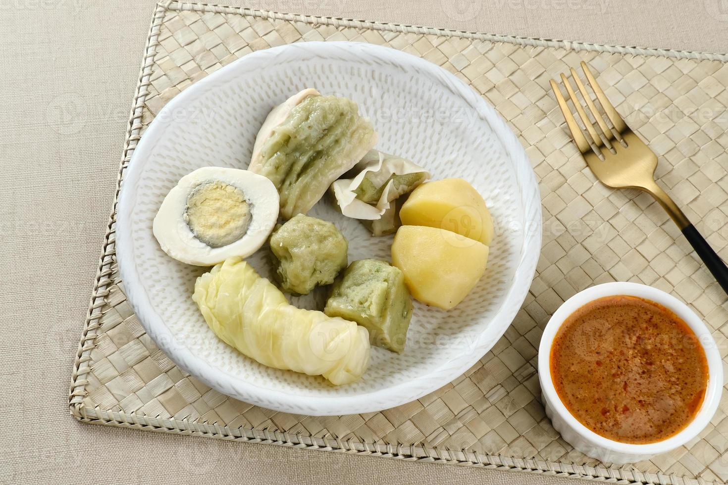 siomay bandung, albóndigas al vapor con huevo cocido, tofu, patatas y rollo de col. Comida callejera tradicional indonesia con salsa de cacahuete y salsa de soja, servida con lima verde. foto