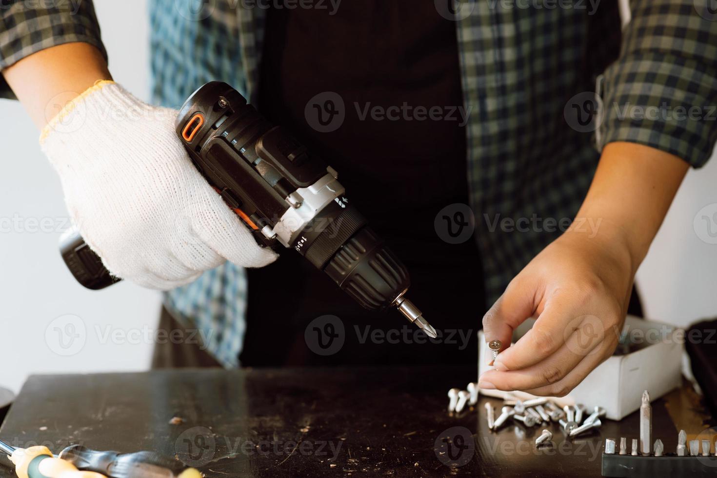 Close up of male mechanic holding electric cordless screwdriver drill with wood screw in the factory. Working with the screw. Professional carpenter. Concept furniture at home. photo