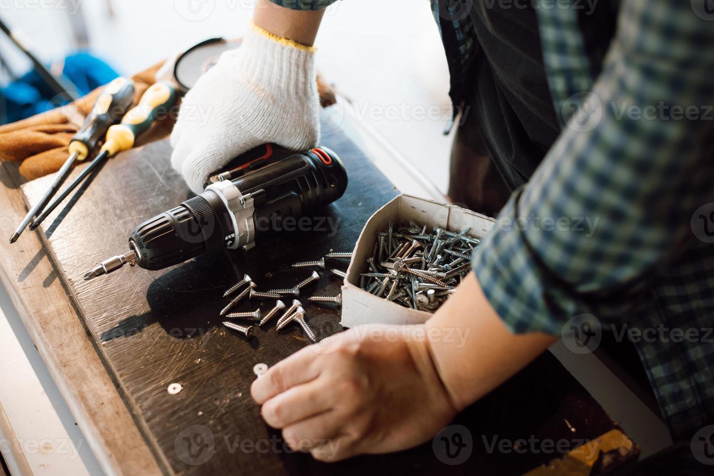 Close up of male mechanic holding electric cordless screwdriver drill with wood screw in the factory. Working with the screw. Professional carpenter. Concept furniture at home. photo