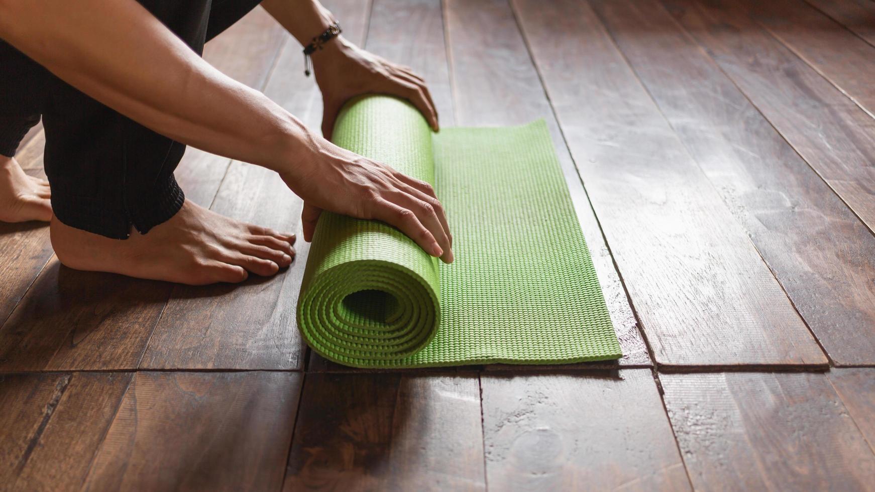 primer plano de un hombre que hace rodar a mano una alfombra de yoga verde o una alfombra de ejercicio después de hacer ejercicio de yoga matutino en casa. vida sana y concepto de vida saludable. foto