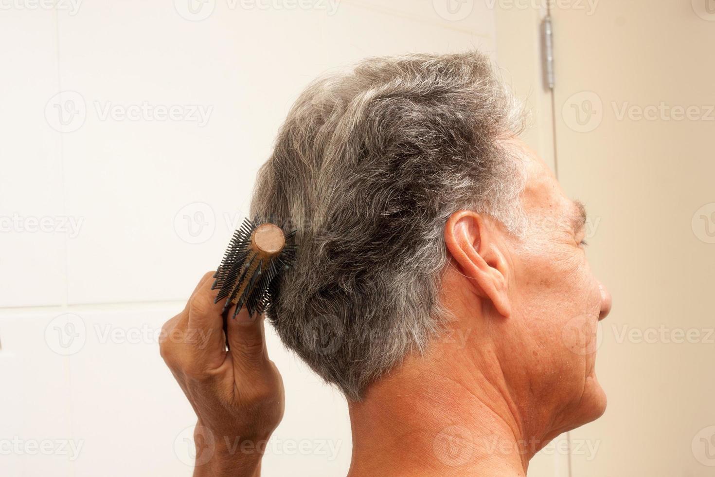 Mature Man 60plus combing his mostly gray hair in the back of his head in front of a mirror photo