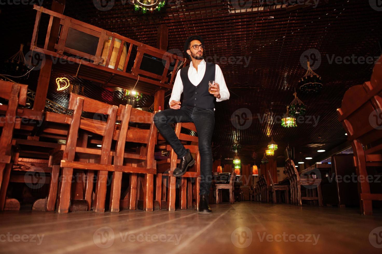 Handsome well-dressed arabian man with glass of whiskey and cigar posed at pub. photo