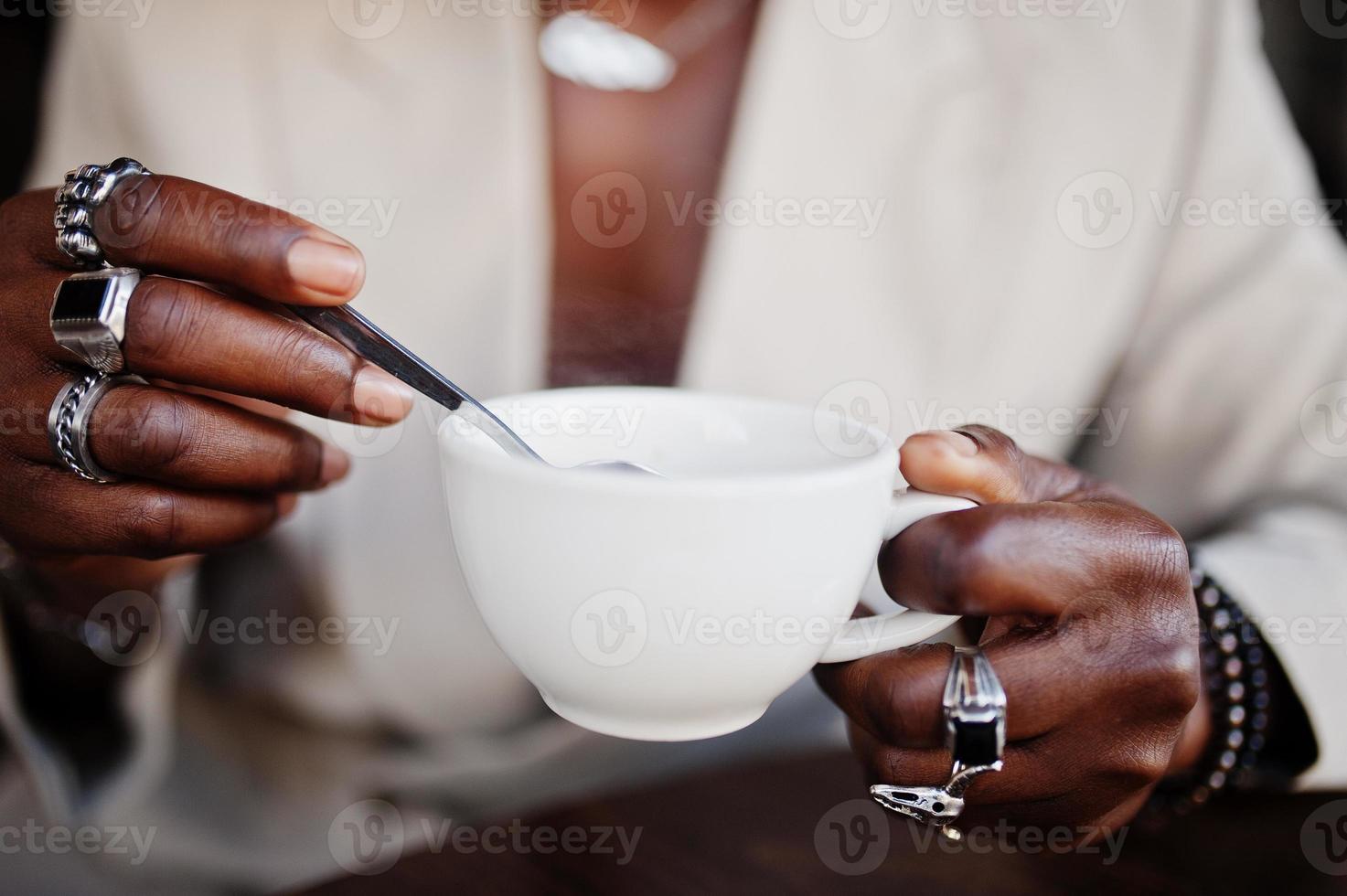 Stylish afro man in beige old school suit sitting on cafe with cup of coffee. Fashionable young African male in casual jacket on bare torso. photo