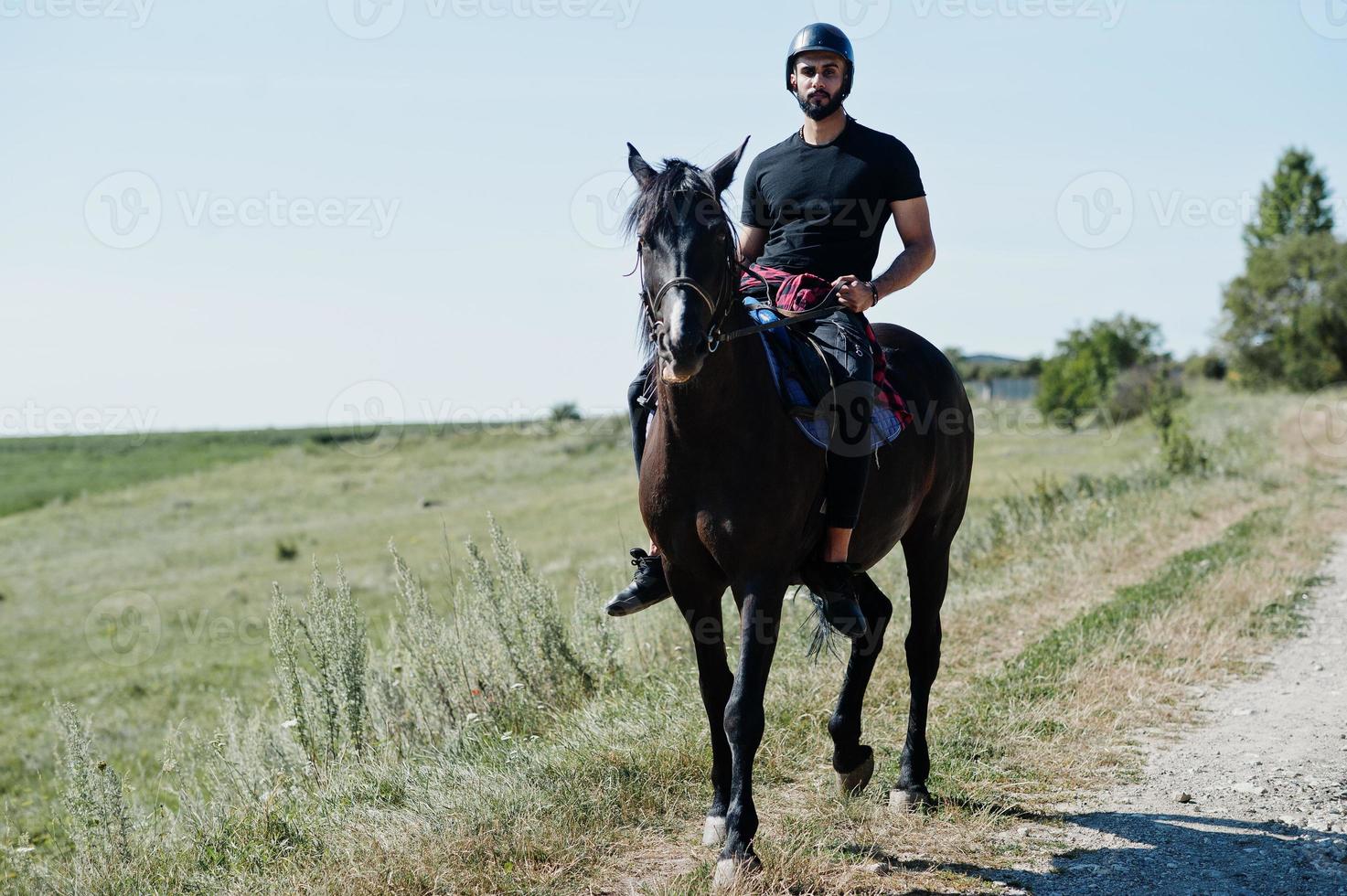 El hombre árabe de barba alta usa casco negro, monta un caballo árabe. foto