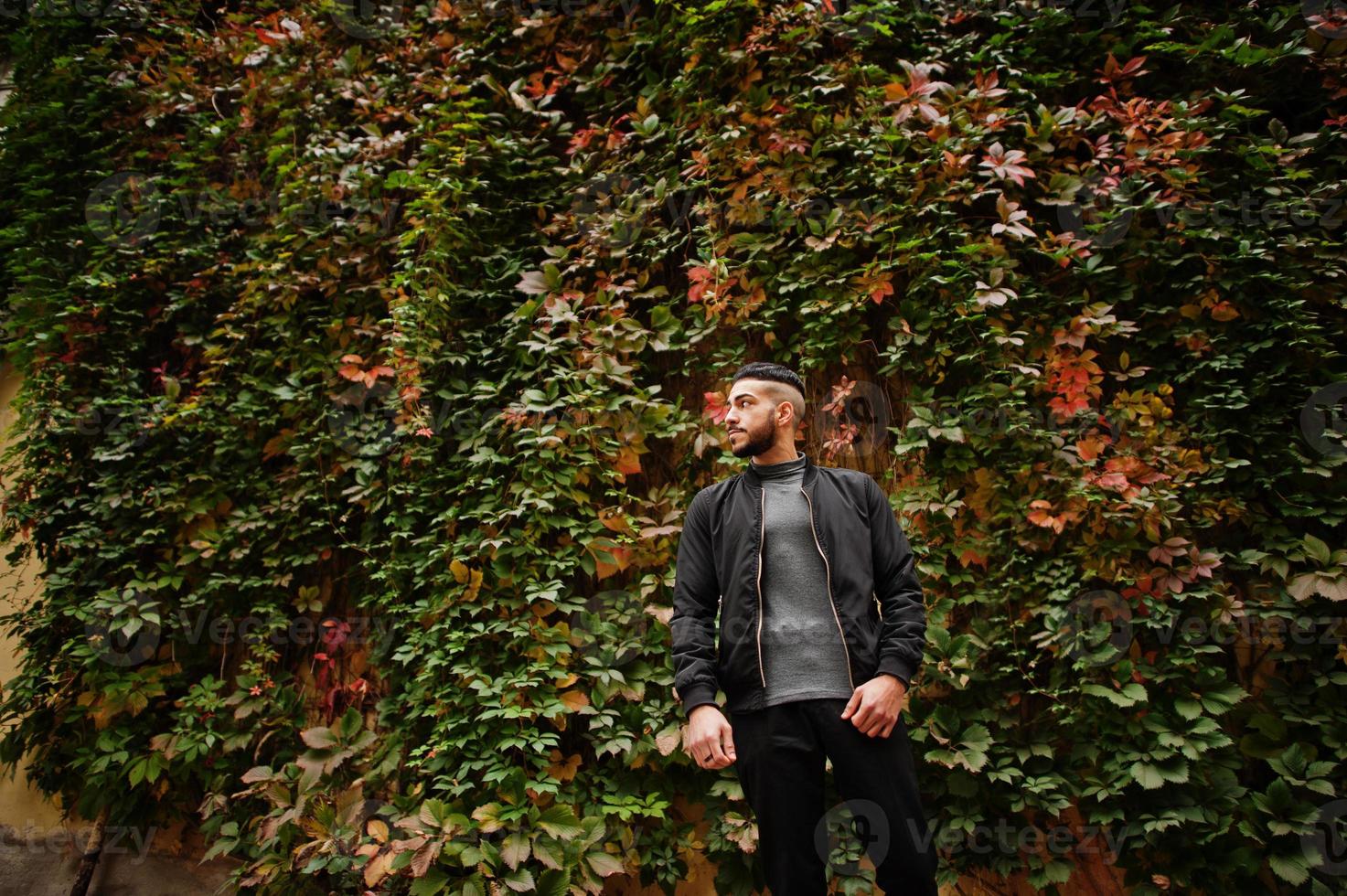 Portrait of stylish arab beard man wear grey turtleneck and black jaket. Arabian model guy on a background of autumn leaves. photo