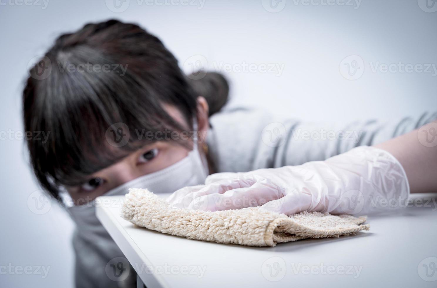 una joven ama de casa está limpiando, limpiando la superficie de la mesa de casa para detener la propagación de la infección con un trapo húmedo, antibacteriano, de cerca, estilo de vida. foto