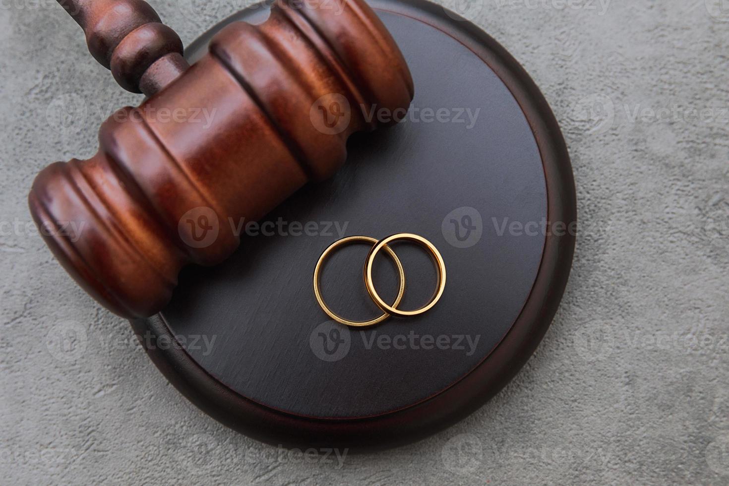 Law theme. Judge gavel wedding rings on concrete stone grey background. Divorce proceedings. Mallet of judge deciding on marriage divorce, marital agreement, legalities of divorce. photo