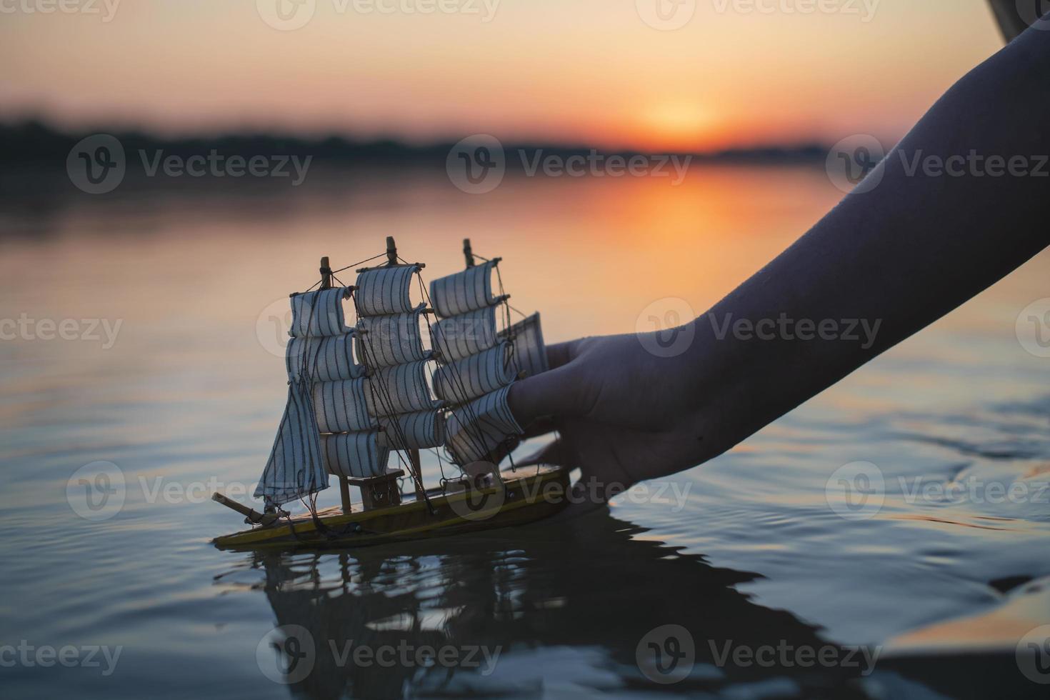 A boy launches a toy decorative ship at sunset. Children's outdoor recreation in summer. photo