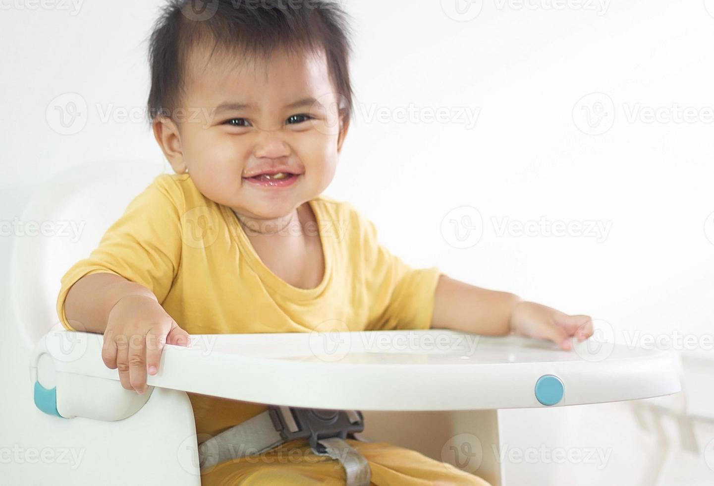 una linda chica blanca sentada en una silla desayunando en el hogar interior alimentando deliciosas comidas que son altamente nutritivas el bebé tiene una cara alegre, divertida, sonriente y feliz en un estilo de vida familiar saludable. foto