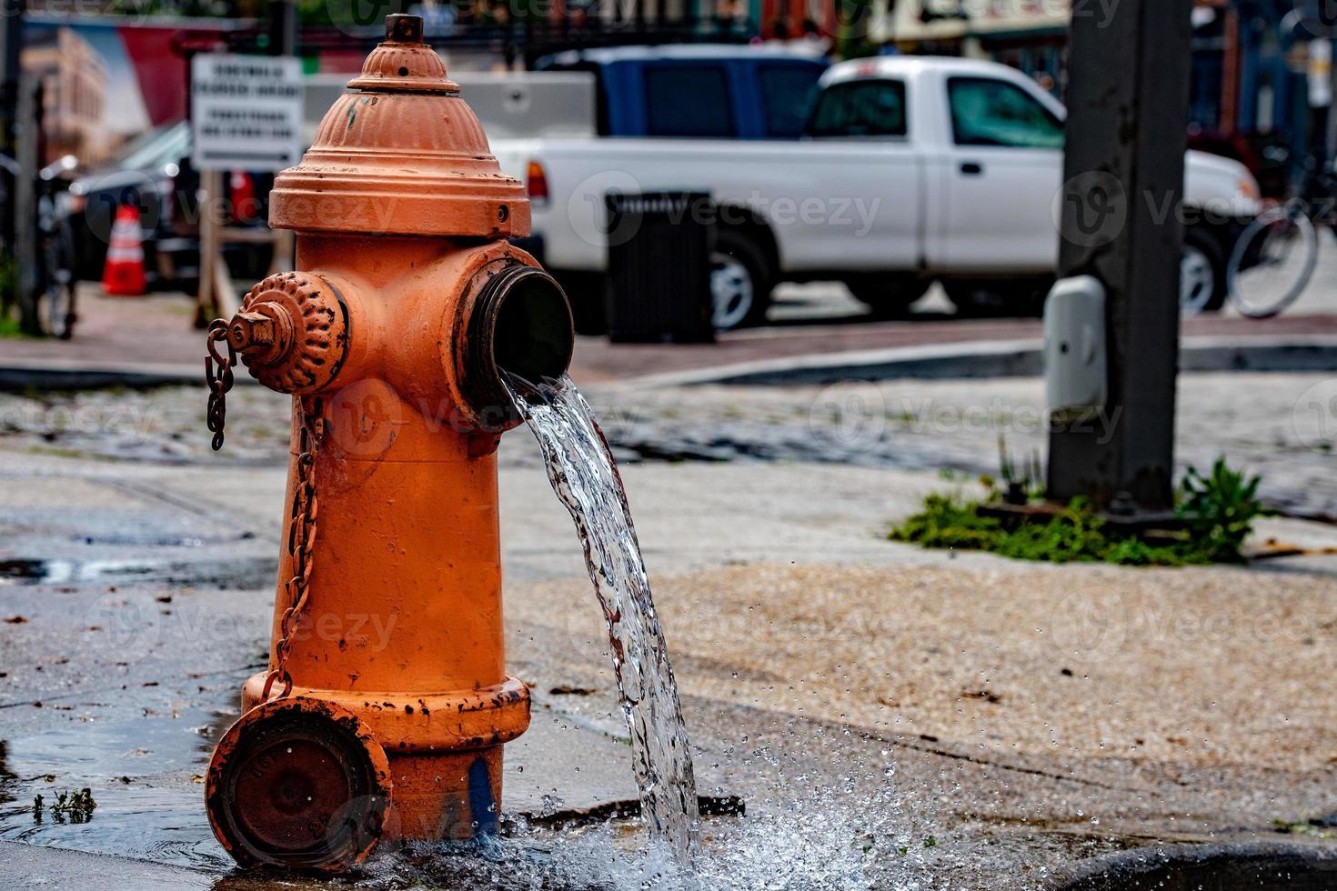 Street orange hydrant spreading water on the street photo