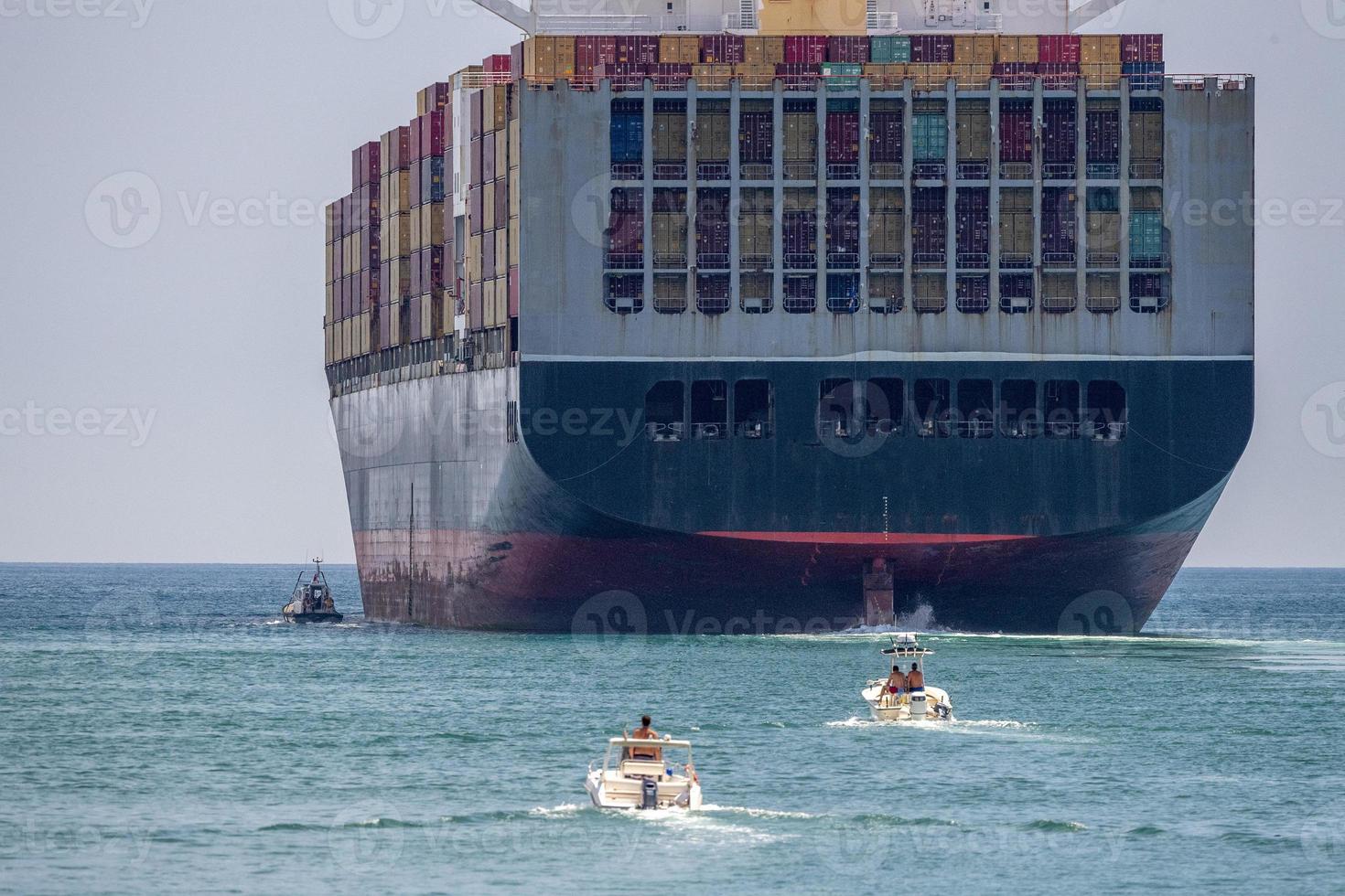 Container ship near the coast with tugboat and small vessels photo