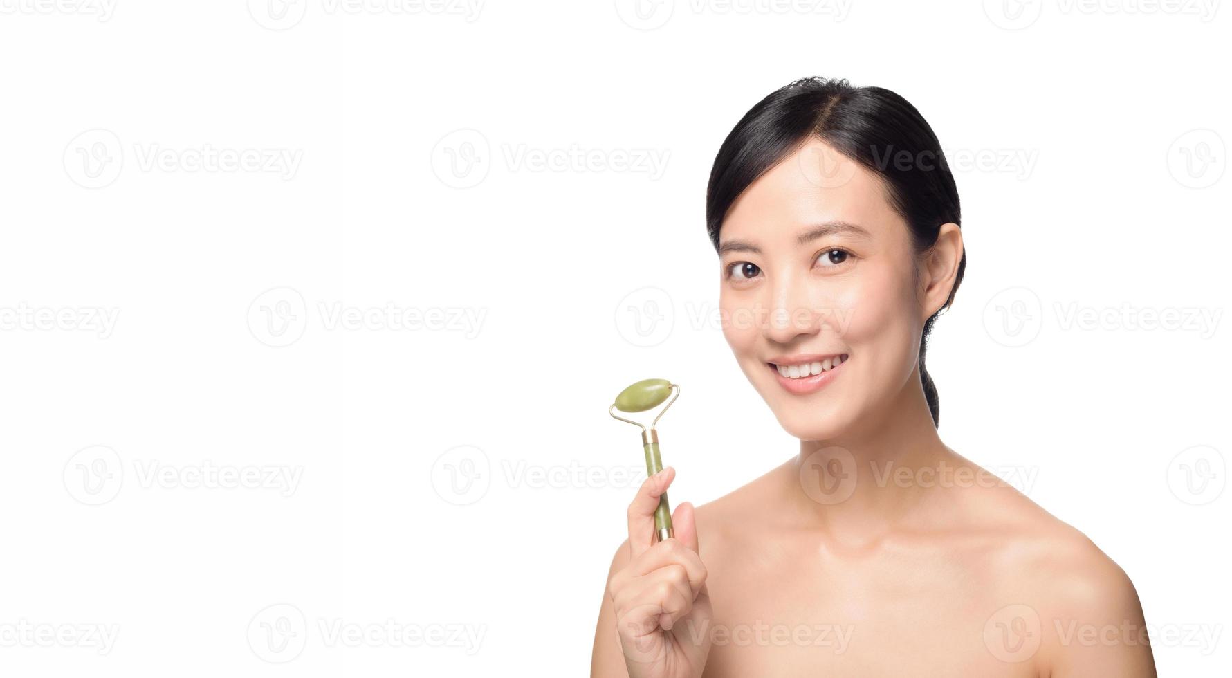 foto de estudio de una atractiva joven asiática usando un rodillo de jade en la cara contra un fondo blanco.