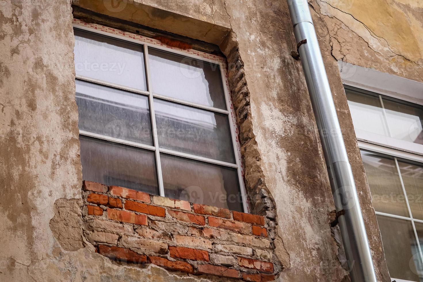 Old dirty wooden window and red brick with plaster wall in old town in Europe photo