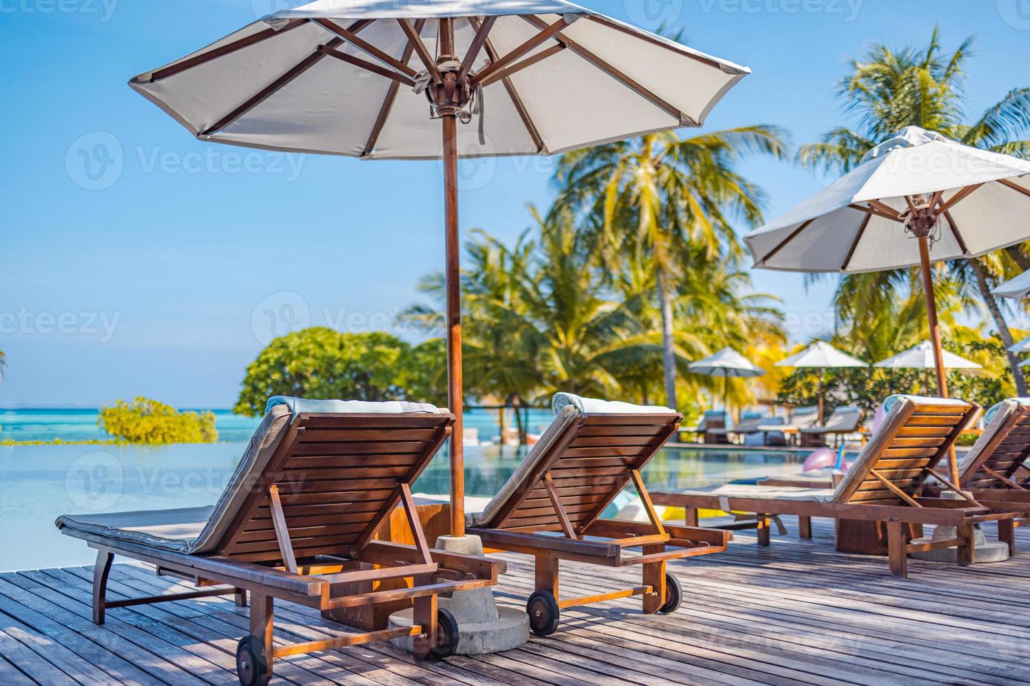 Umbrellas and chairs around outdoor swimming pool in resort hotel for vacation leisure lifestyle. Luxury destination concept, lounge closeup scenic under palm trees, relax, tranquil vibes photo