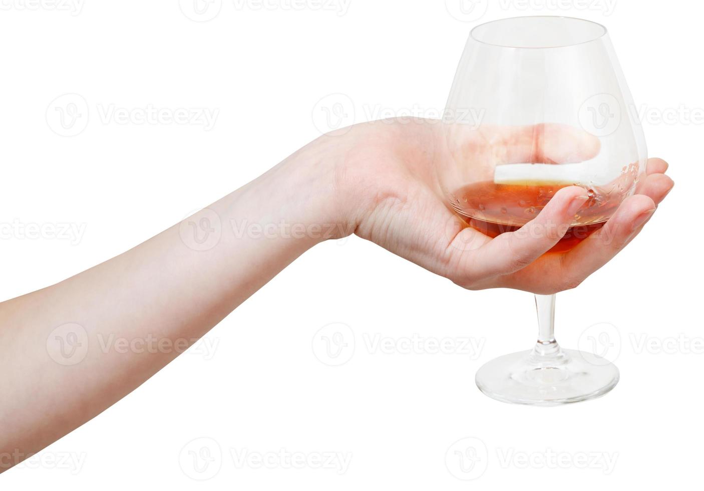 hand holds glass goblet with cognac isolated photo