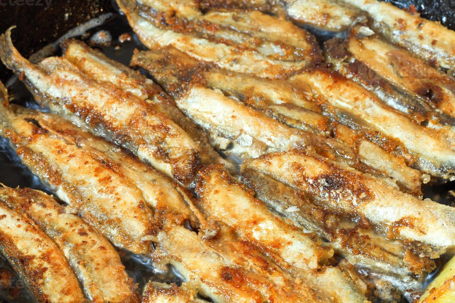 fried fish capelin on black frying pan photo