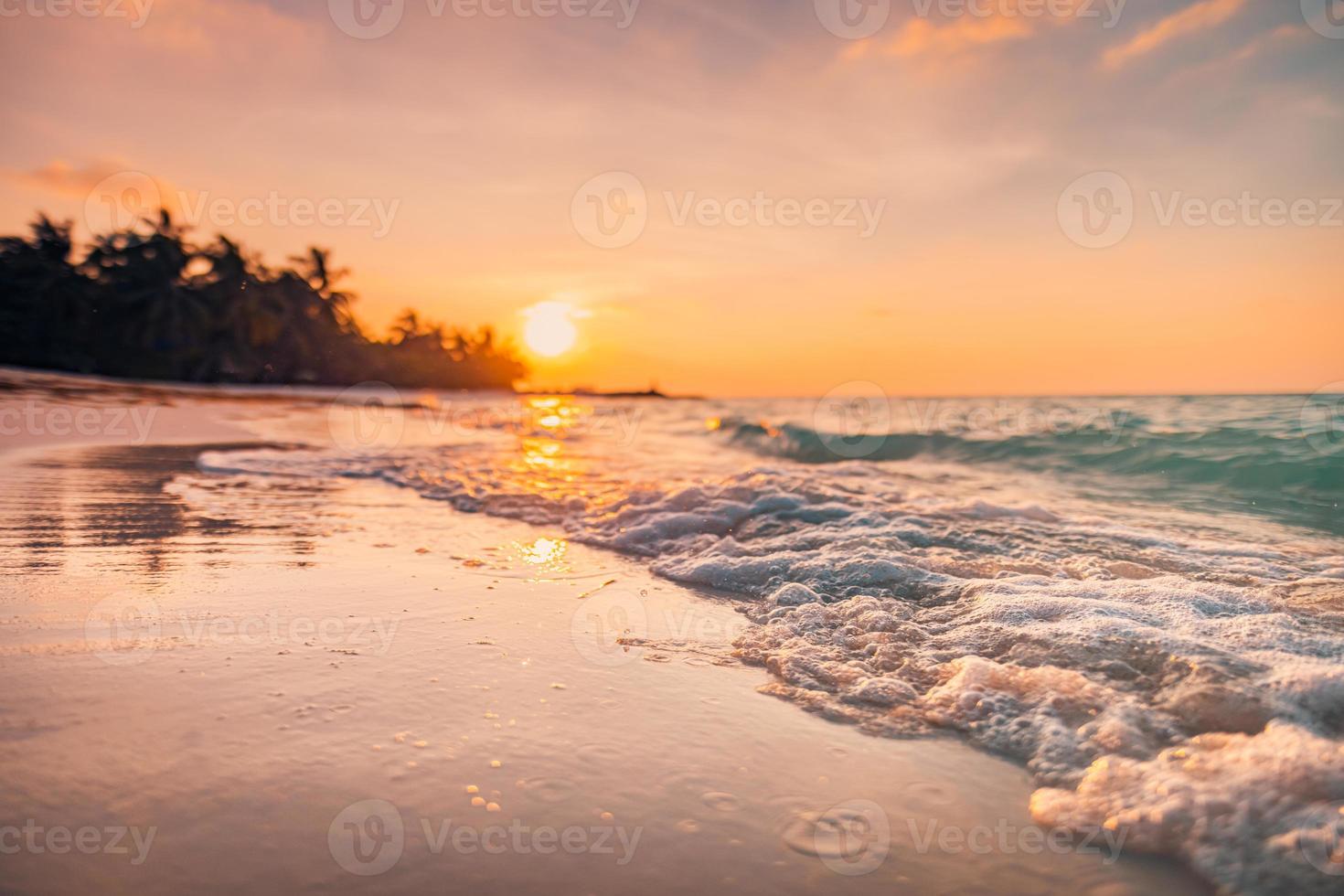 hermosa puesta de sol borrosa sobre la playa del paraíso tropical, salpicaduras de olas. tranquilas vacaciones de verano o paisaje de vacaciones. silueta relajante de palmeras en la playa al atardecer, naturaleza exótica del mar en calma. playa de ensueño foto