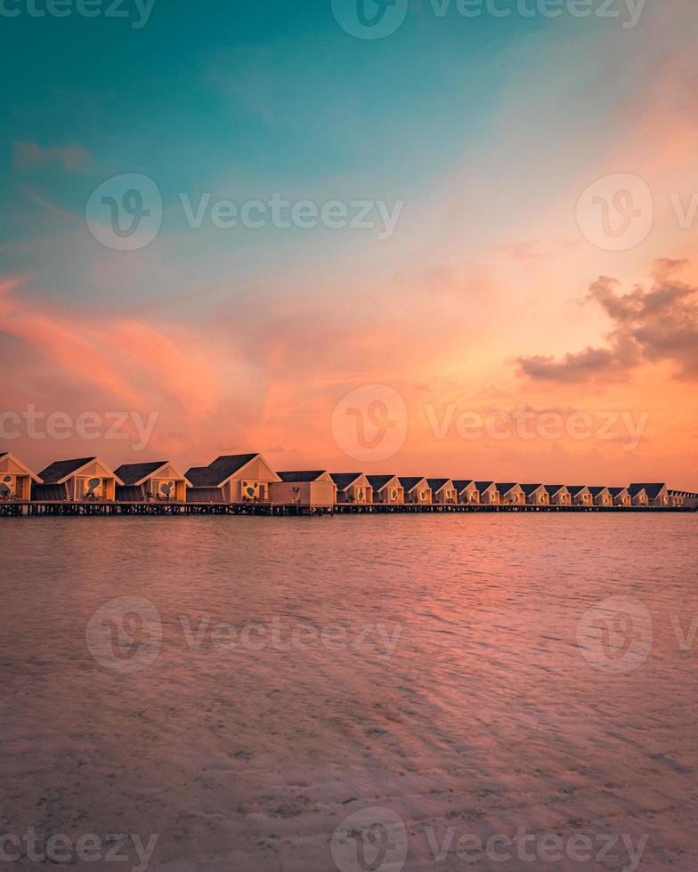 Maldives island sunset. Water bungalows resort at islands beach. Indian Ocean, Maldives. Beautiful sunset landscape, luxury resort villas and colorful sky. Summer vacation holiday and travel concept photo