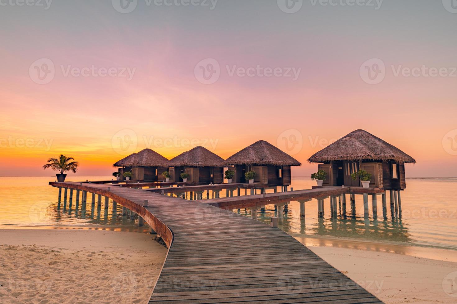 puesta de sol en la isla de maldivas. resort de bungalows de agua en la playa de las islas. océano índico, maldivas. hermoso paisaje de puesta de sol, villas de resort de lujo y cielo colorido. concepto de vacaciones y viajes de vacaciones de verano foto