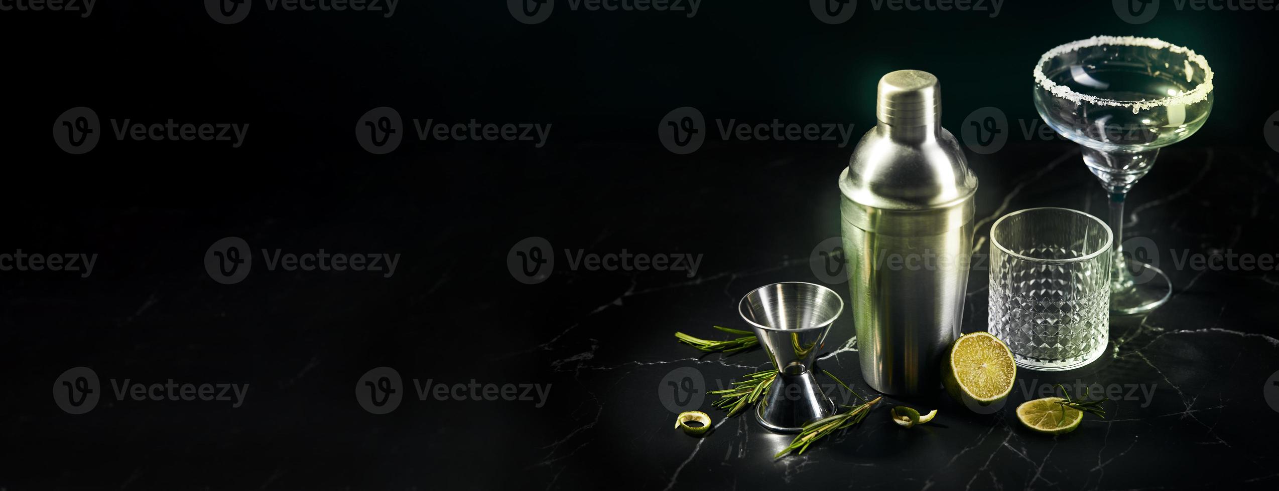 Cocktail shaker and cocktail glasses, and ingredients on dark marble background photo