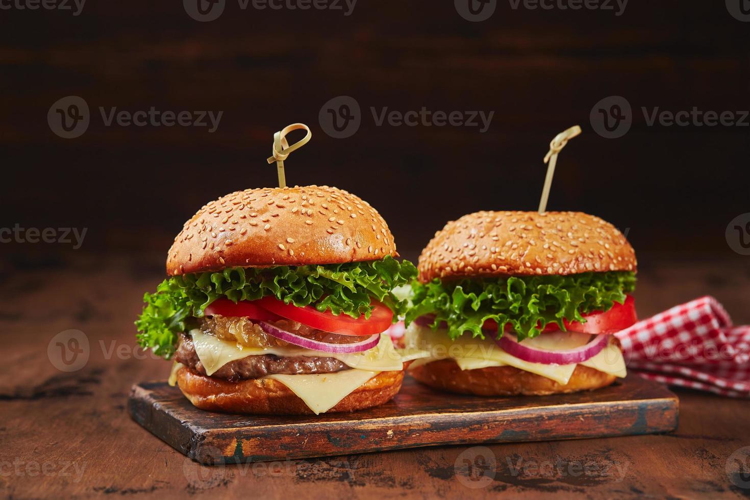dos hamburguesas caseras con mermelada de carne, queso y cebolla en una tabla de madera. concepto de comida rápida, comida americana foto