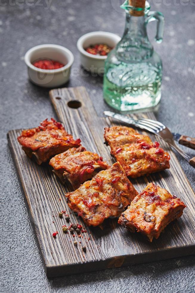 Grilled baked pork ribs with spices on wooden cutting board on dark background. American food concept. photo