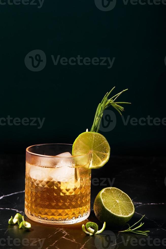 cóctel alcohólico o no alcohólico con lima y romero sobre una mesa de mármol oscuro foto