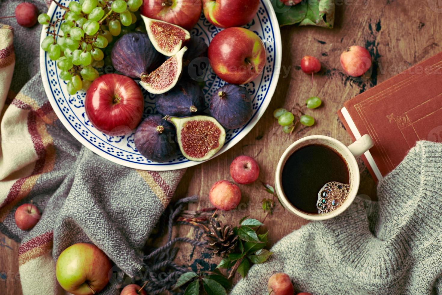 plato con higos, manzanas y uvas y taza de café sobre fondo de madera con suéter cálido, bufanda, hojas de otoño y manzanas. fondo de otoño, vista superior. foto